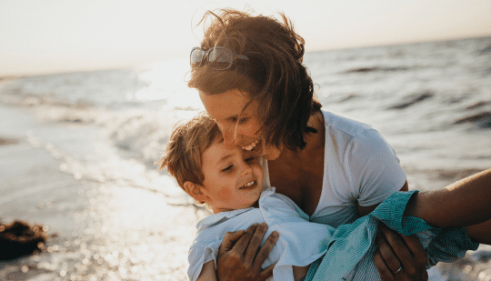 A joyful moment of a woman hugging a child by the seaside at sunset