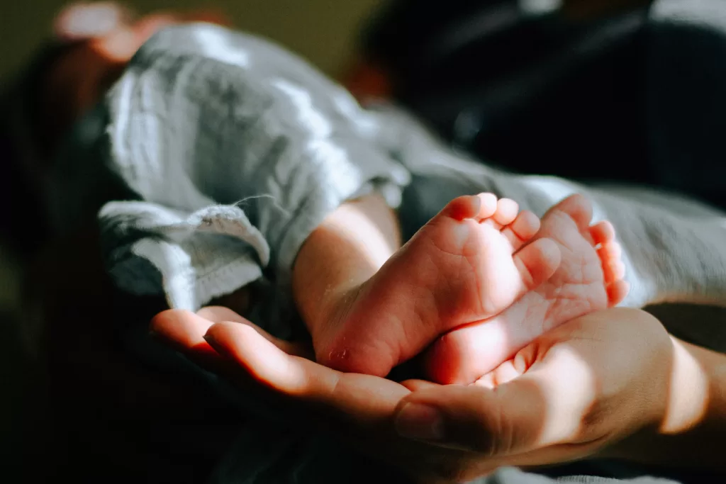 Close-up of a newborn's bare feet cradled gently in an adult's hands, symbolizing delicate care and protection.