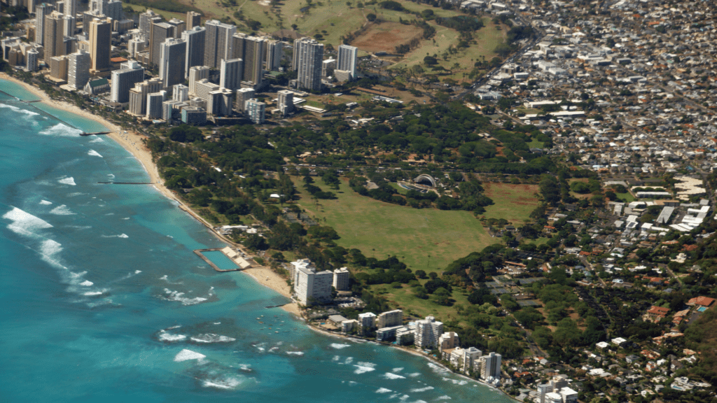 A picturesque view of Kahala, Hawaii, featuring golden sandy beaches, clear turquoise waters, and lush greenery with luxurious beachfront homes in the background.